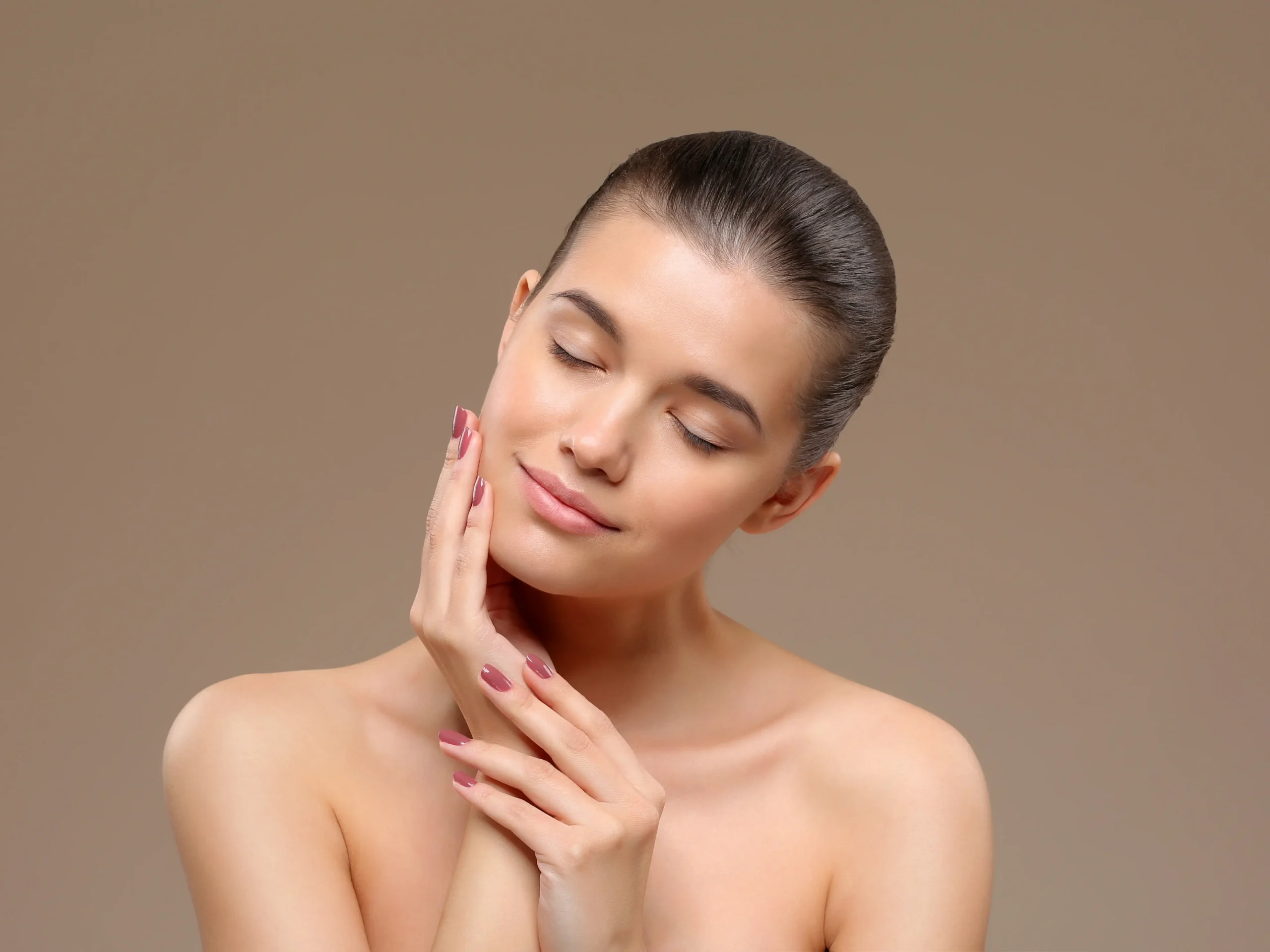Woman with eyes closed gently touching her cheek against a neutral background