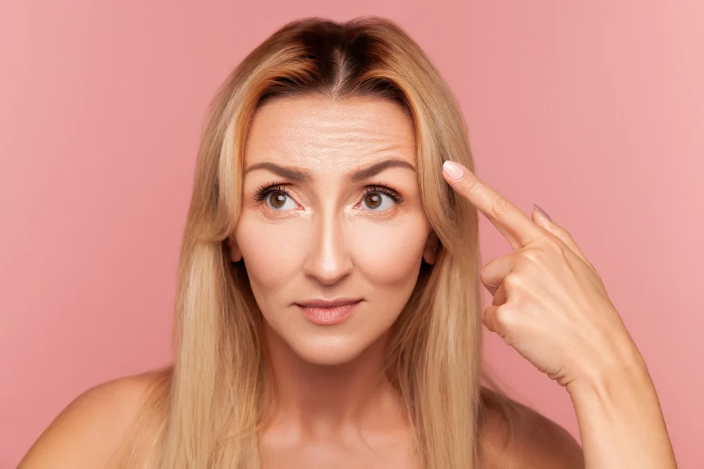 Person pointing to visible forehead lines while facing the camera